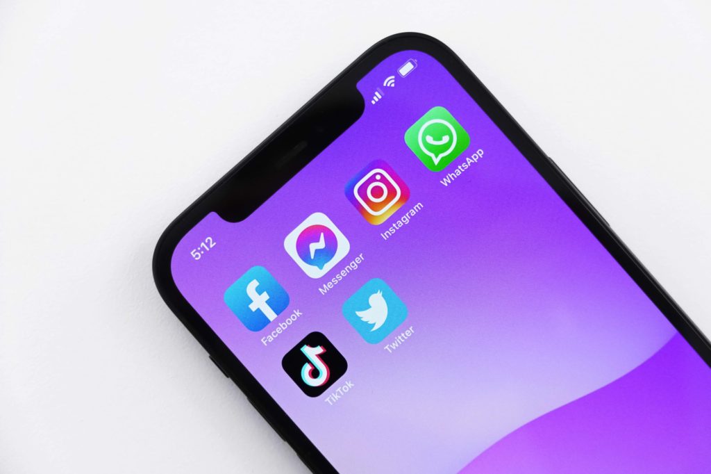 iPhone with 6 social media apps on a purple background screen